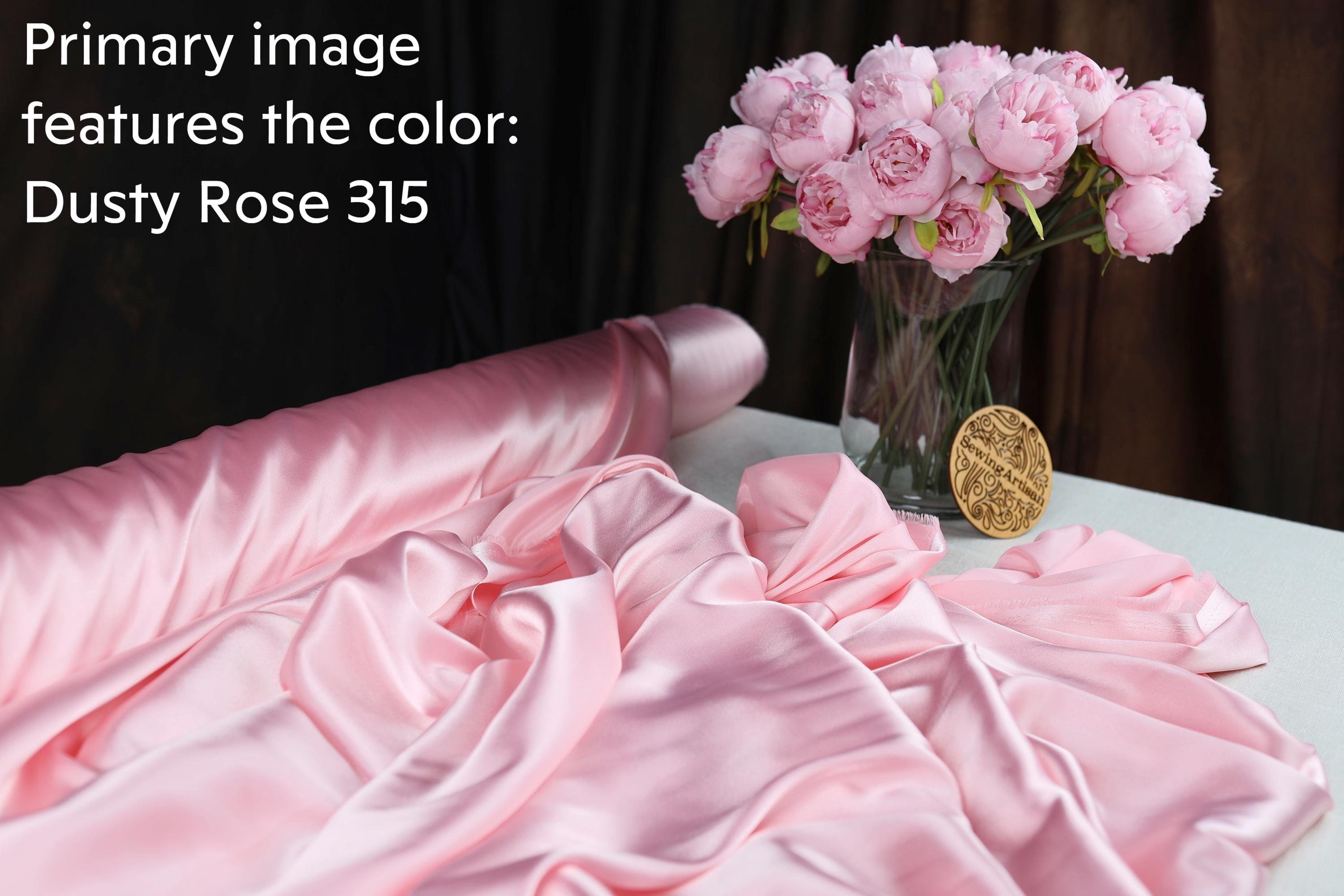 a bouquet of pink roses in a glass vase, along with a roll of pink satin fabric and a gold medallion.