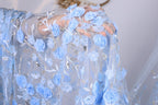 A close-up view of a hand holding a delicate, intricately embroidered fabric with blue flowers and leaves.