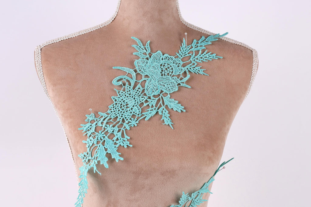 A mannequin torso wearing a teal-colored lace piece with intricate floral patterns.