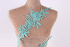 A mannequin torso wearing a teal-colored lace piece with intricate floral patterns.