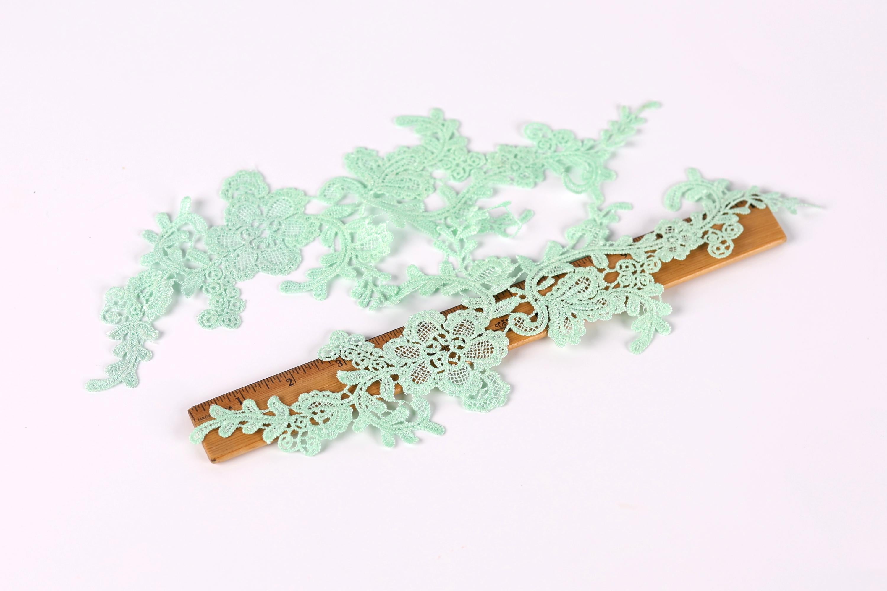 a collection of small, delicate green lace pieces arranged on a wooden ruler, which is placed on a white background.