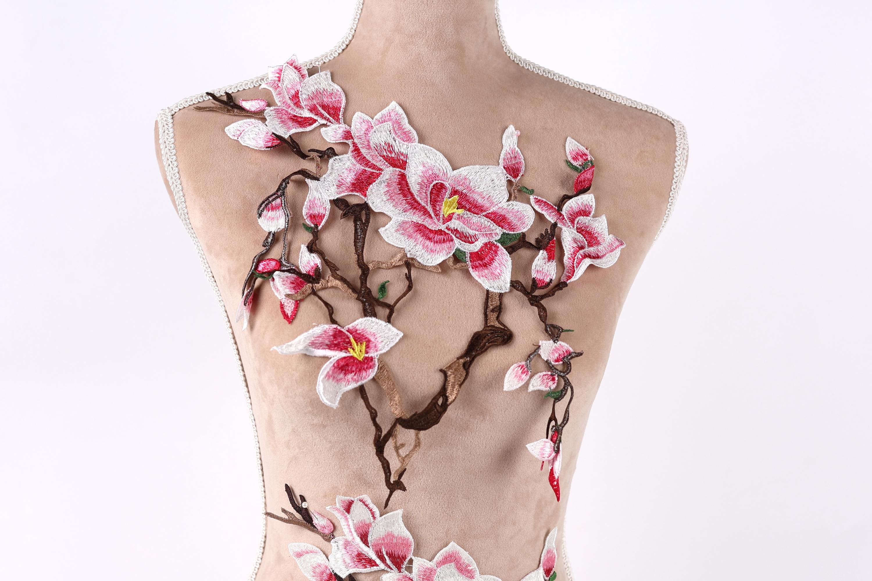 A mannequin torso with a floral embroidered design on it, featuring pink and white flowers and branches.