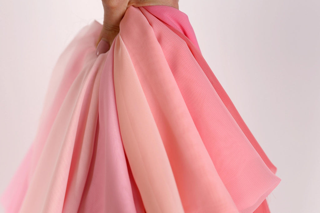 A hand is holding a bunch of pink and peach fabric, with the fabric appearing to be folded or draped.