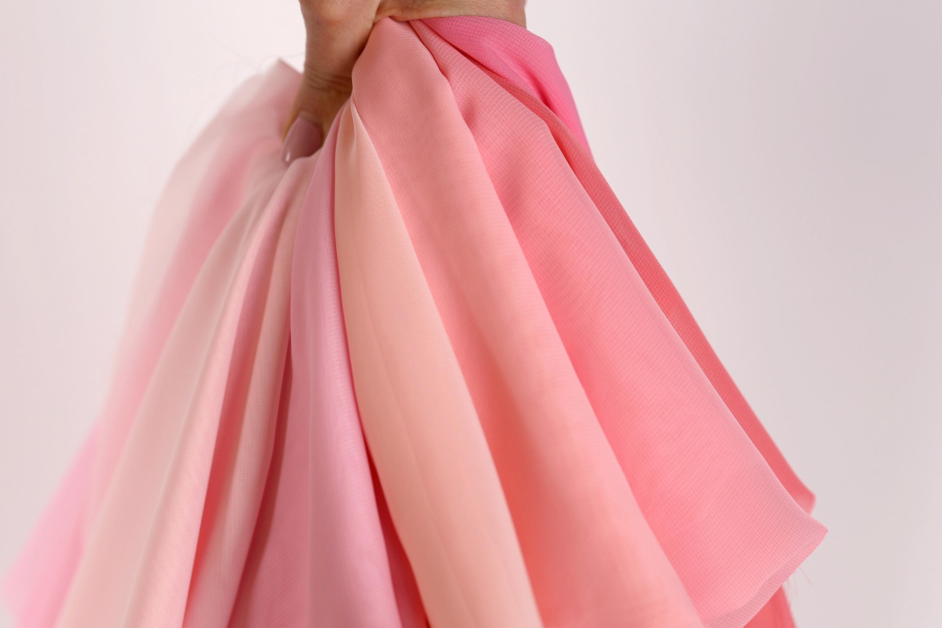 A hand is holding a bunch of pink and peach fabric, with the fabric appearing to be folded or draped.