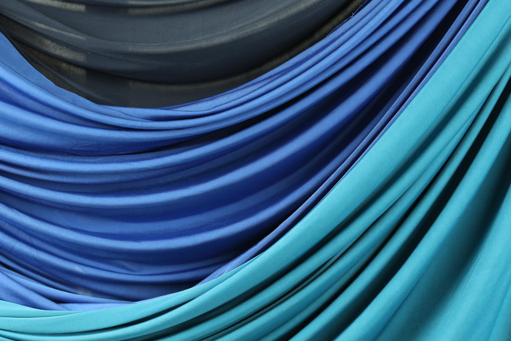 a close-up view of a fabric with a blue and teal color scheme, featuring a mix of blue and teal hues. The fabric appears to be folded or draped, creating a visually interesting and textured appearance.