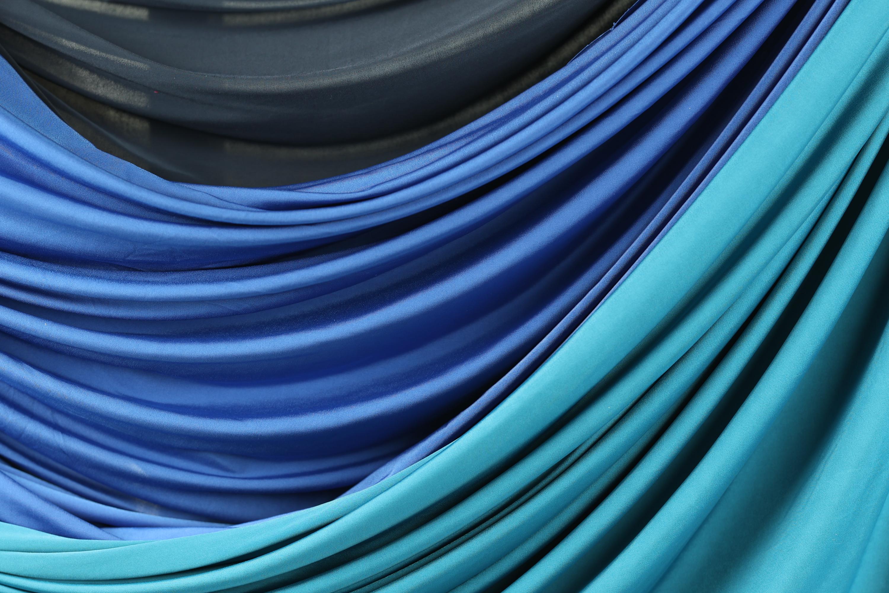 a close-up view of a fabric with a blue and teal color scheme, featuring a mix of blue and teal hues. The fabric appears to be folded or draped, creating a visually interesting and textured appearance.