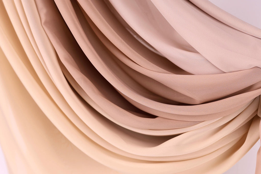 a close-up view of a fabric with a gradient of colors, transitioning from a light beige to a darker beige. The fabric appears to be made of a soft, flowing material, possibly silk or chiffon. The colors and texture of the fabric create a visually appealing and textured appearance.