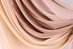 a close-up view of a fabric with a gradient of colors, transitioning from a light beige to a darker beige. The fabric appears to be made of a soft, flowing material, possibly silk or chiffon. The colors and texture of the fabric create a visually appealing and textured appearance.