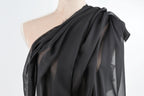 A mannequin wearing a black, sheer fabric draped over its shoulder.