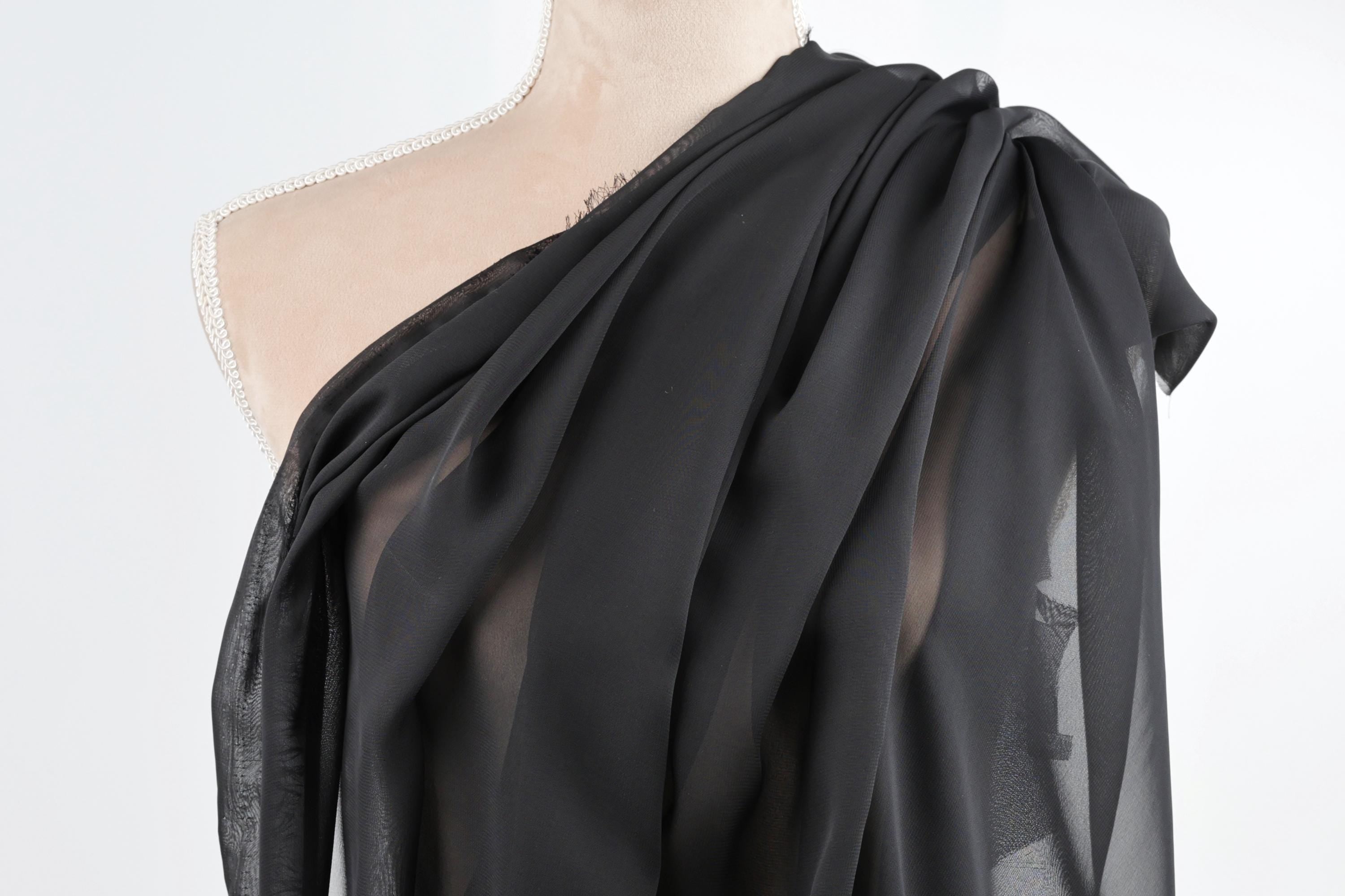 A mannequin wearing a black, sheer fabric draped over its shoulder.