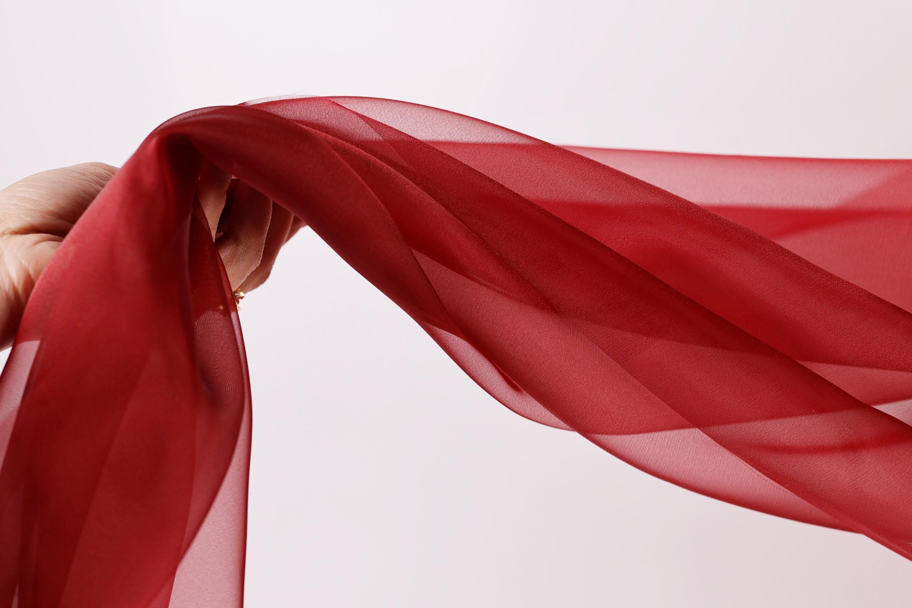 A hand is holding a red fabric, which appears to be a sheer or sheer-like material, and it is being twisted or curled.