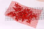 a red floral embroidered piece of fabric with a flower and leaves, placed on a transparent ruler.