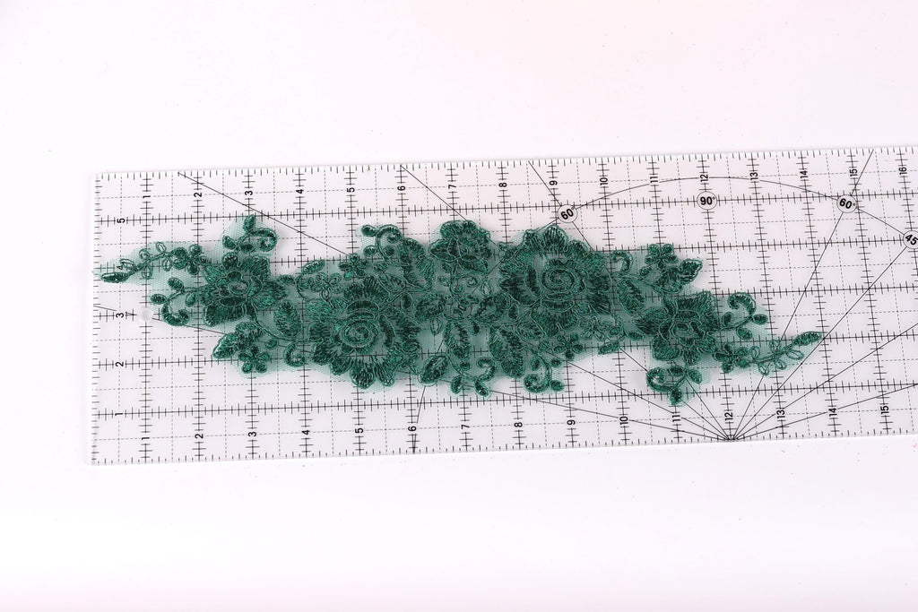a green lace-like fabric placed on a transparent ruler, which is placed on a white surface.