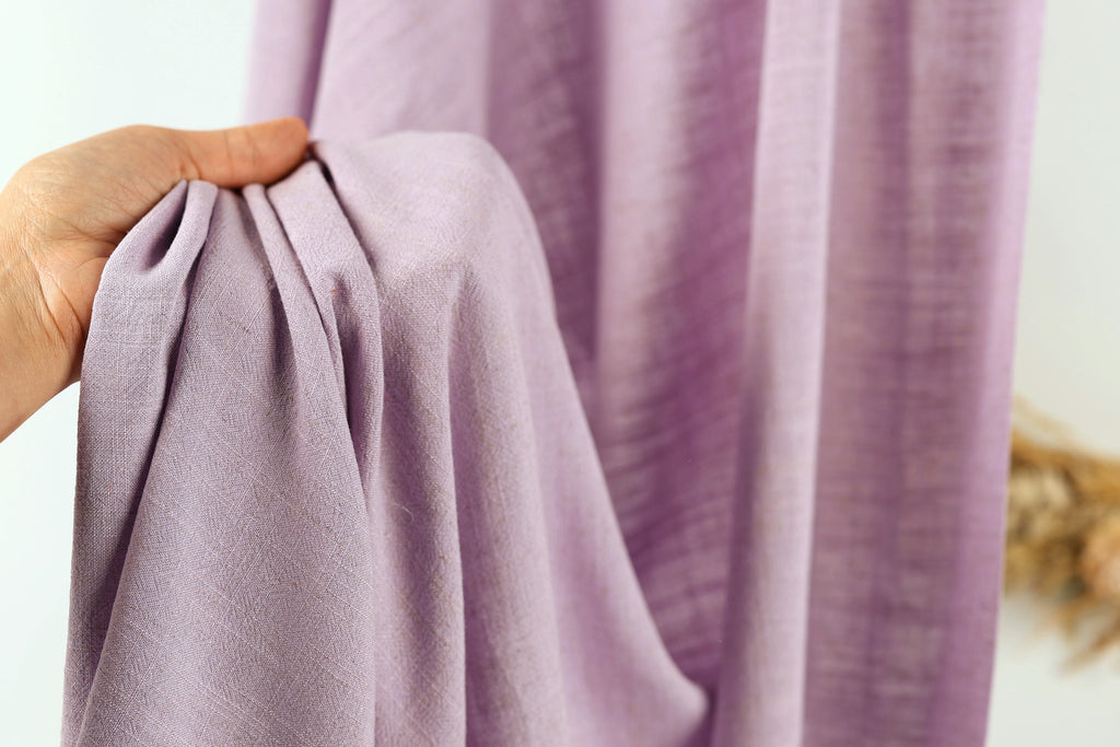 A hand is holding a folded purple fabric, which appears to be a piece of clothing or textile.