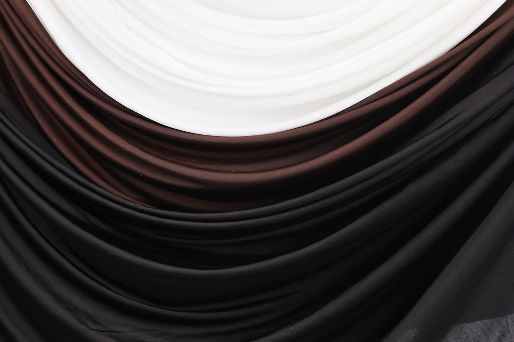 a close-up view of a fabric with a gradient of colors, including black, brown, and white. The fabric appears to be made of a soft, flowing material, possibly silk or chiffon. The colors are layered and interwoven, creating a visually appealing and textured appearance.