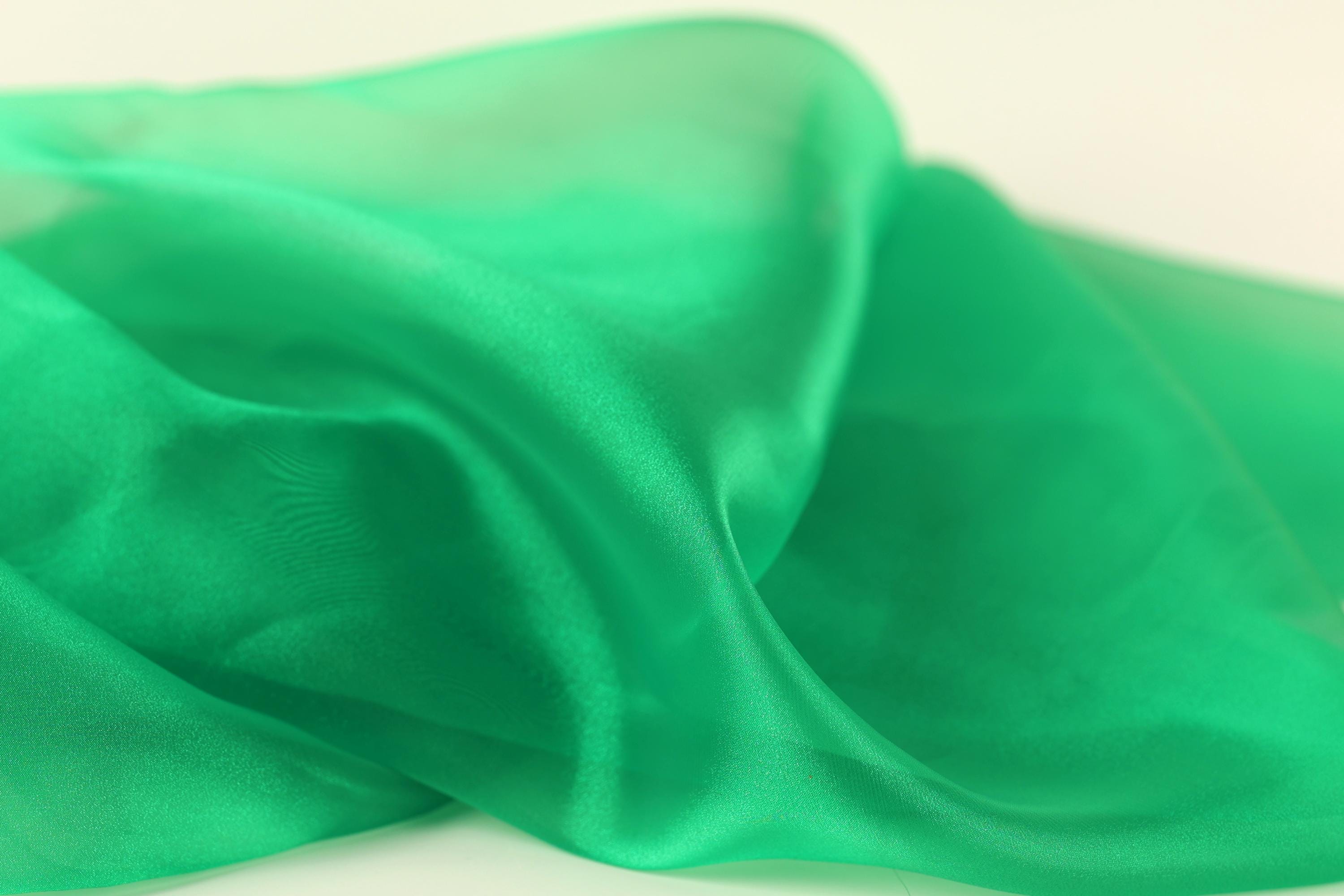 a close-up view of a green fabric, possibly silk or chiffon, with a smooth and shiny texture.