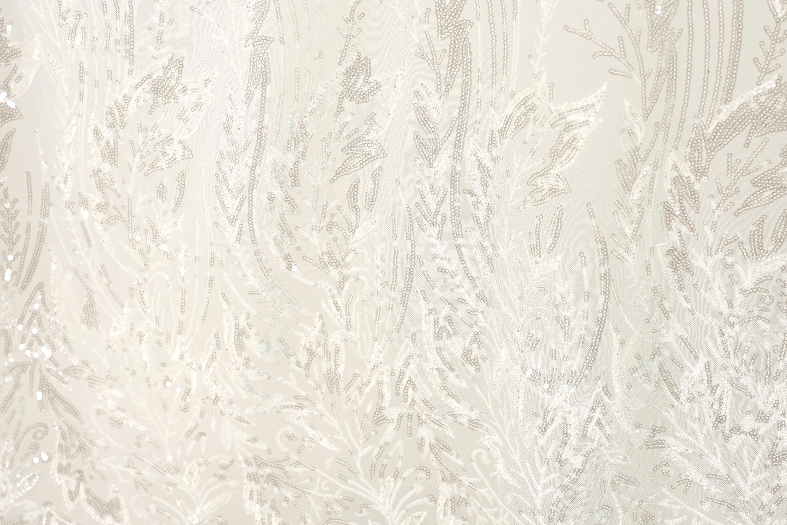 The image is a close-up of a fabric with a white and beige floral pattern, featuring a repeating design of leaves and branches.
