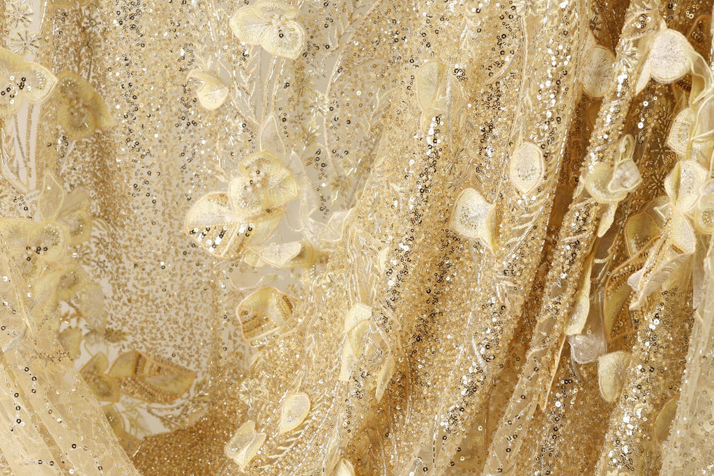 The image is a close-up of a fabric with a gold and white color scheme, featuring a floral pattern and sequin accents.