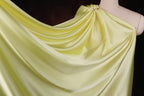 A close-up view of a yellow satin fabric draped over a mannequin, showcasing its smooth and flowing texture.