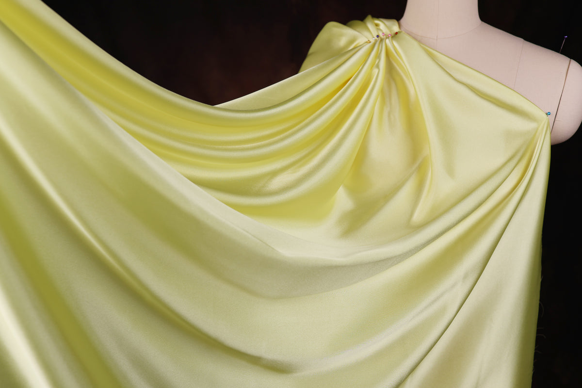 A close-up view of a yellow satin fabric draped over a mannequin, showcasing its smooth and flowing texture.
