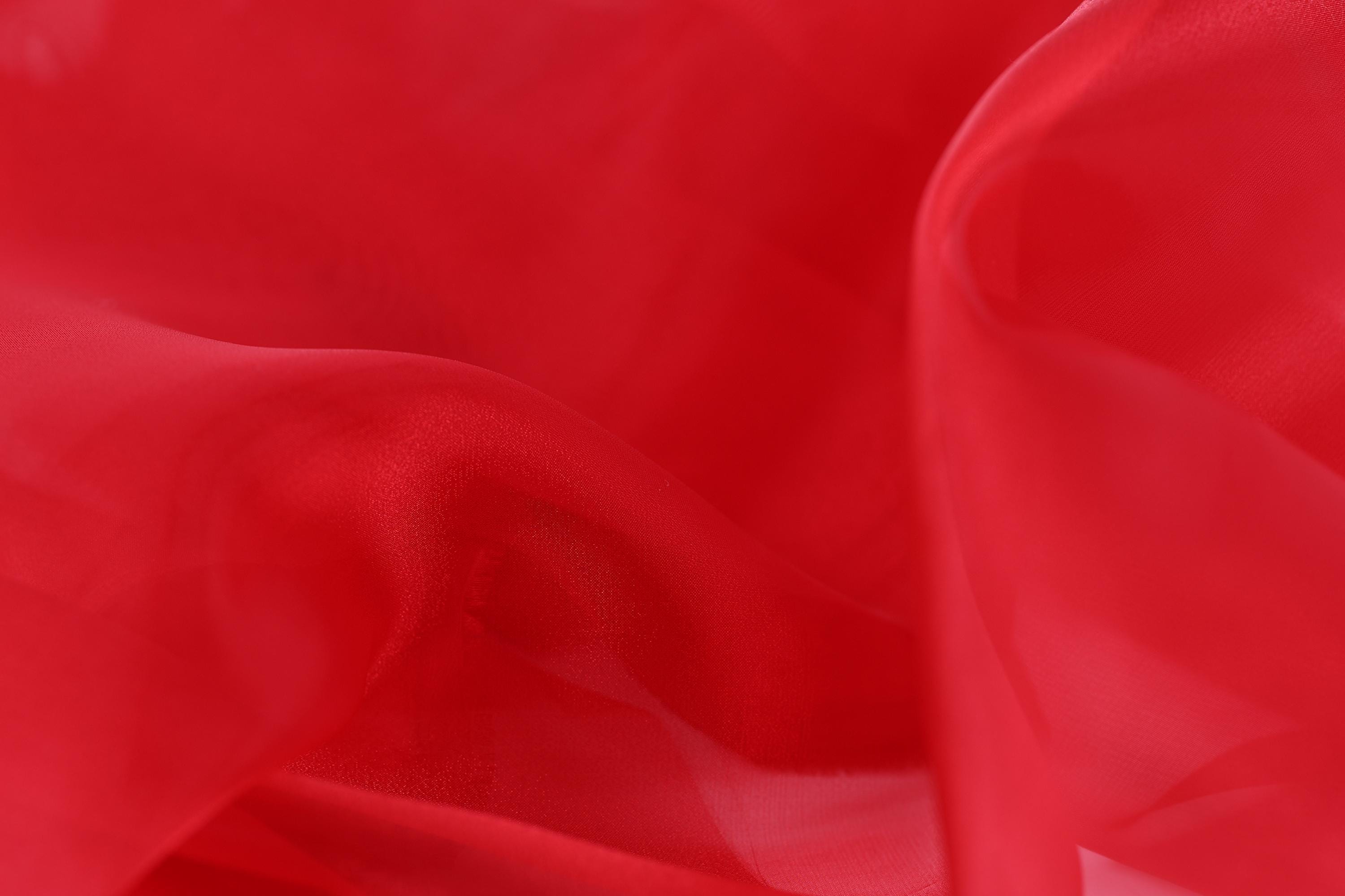 The image is a close-up of a red fabric, possibly silk or chiffon, with a smooth and flowing texture.