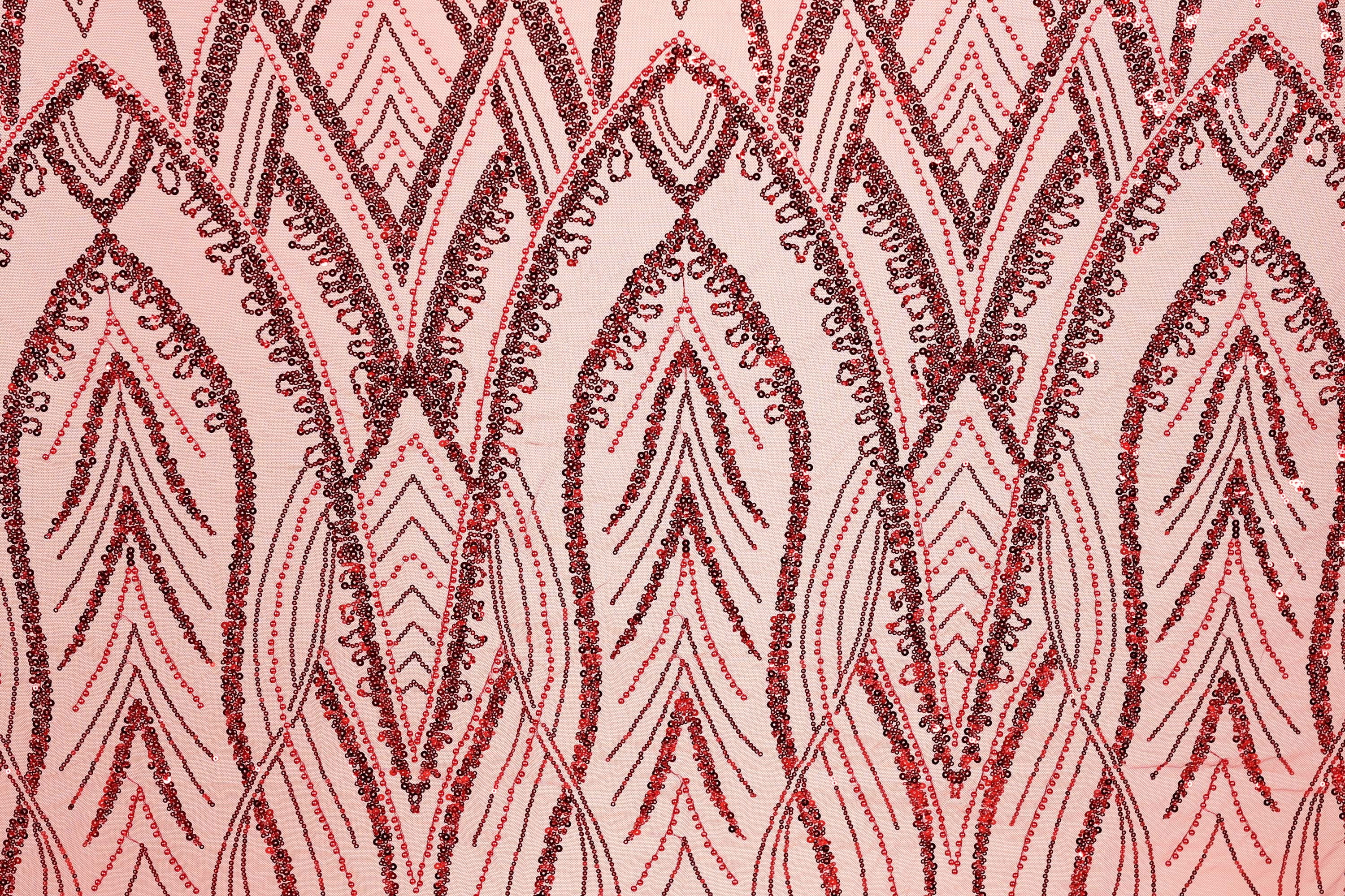 a close-up view of a fabric with a repeating pattern of red and black sequin designs. The pattern consists of various shapes and lines, creating a visually striking and intricate design.