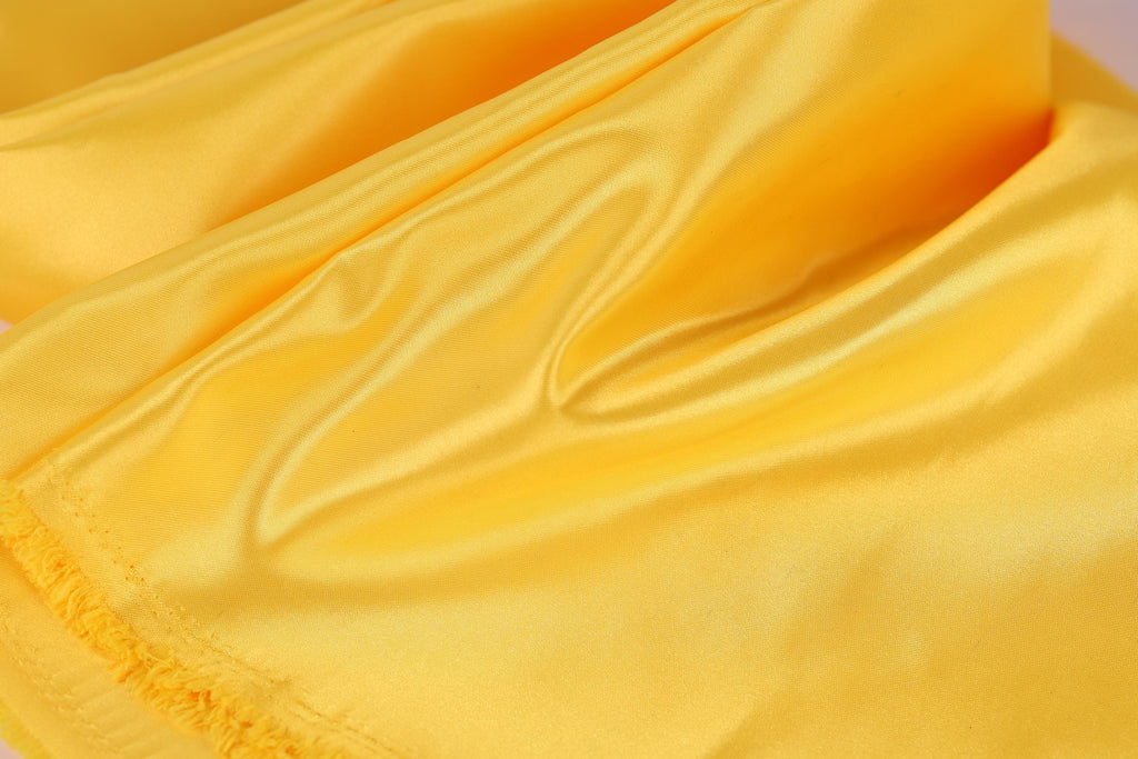 A close-up view of a yellow fabric, possibly silk or satin, with a smooth and shiny texture.