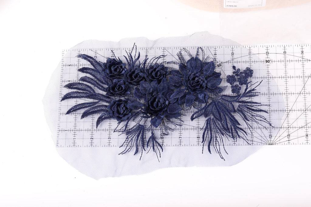 a close-up view of a piece of fabric with a floral design, including blue flowers and leaves. The fabric appears to be a lace or a similar type of material, and it is placed on a white surface. There is a ruler visible in the image, which is likely used for measuring or cutting the fabric.