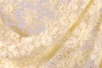 a close-up view of a fabric with a delicate, intricate floral pattern. The fabric appears to be made of a light-colored material, possibly silk or chiffon, with small white flowers or leaves scattered throughout the fabric. The fabric has a slightly wrinkled texture, giving it a soft and delicate appearance.