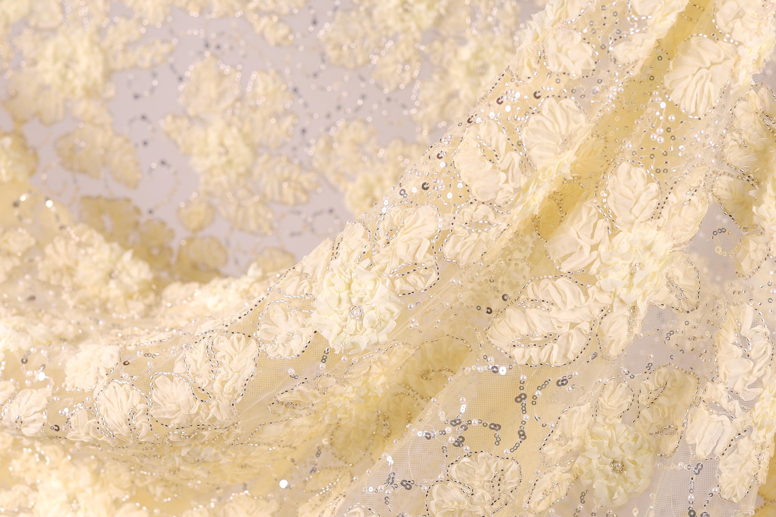 a close-up view of a fabric with a delicate, intricate floral pattern. The fabric appears to be made of a light-colored material, possibly silk or chiffon, with small white flowers or leaves scattered throughout the fabric. The fabric has a slightly wrinkled texture, giving it a soft and delicate appearance.
