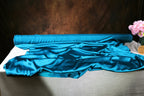 a roll of blue satin fabric on a table, with a vase of pink flowers placed next to it.