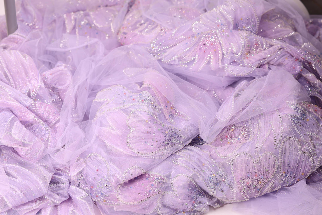 The image is a close-up of a fabric with a purple and white color scheme, featuring a delicate, intricate design with sequins and beads.