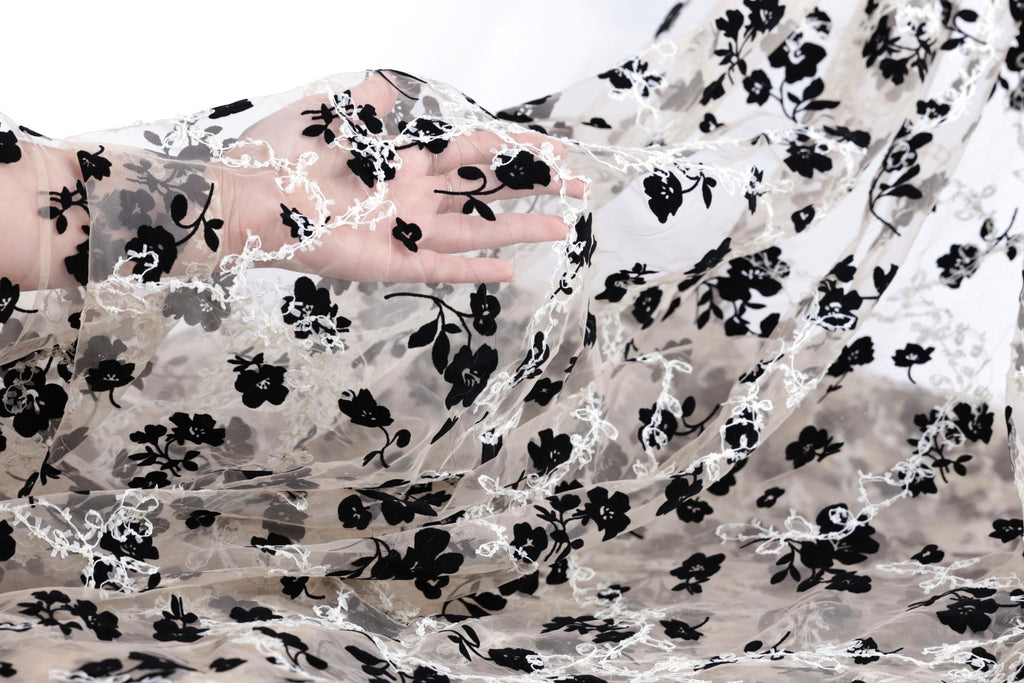 A hand is holding a piece of sheer fabric with a black and white floral pattern.