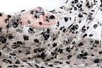 A hand is holding a piece of sheer fabric with a black and white floral pattern.