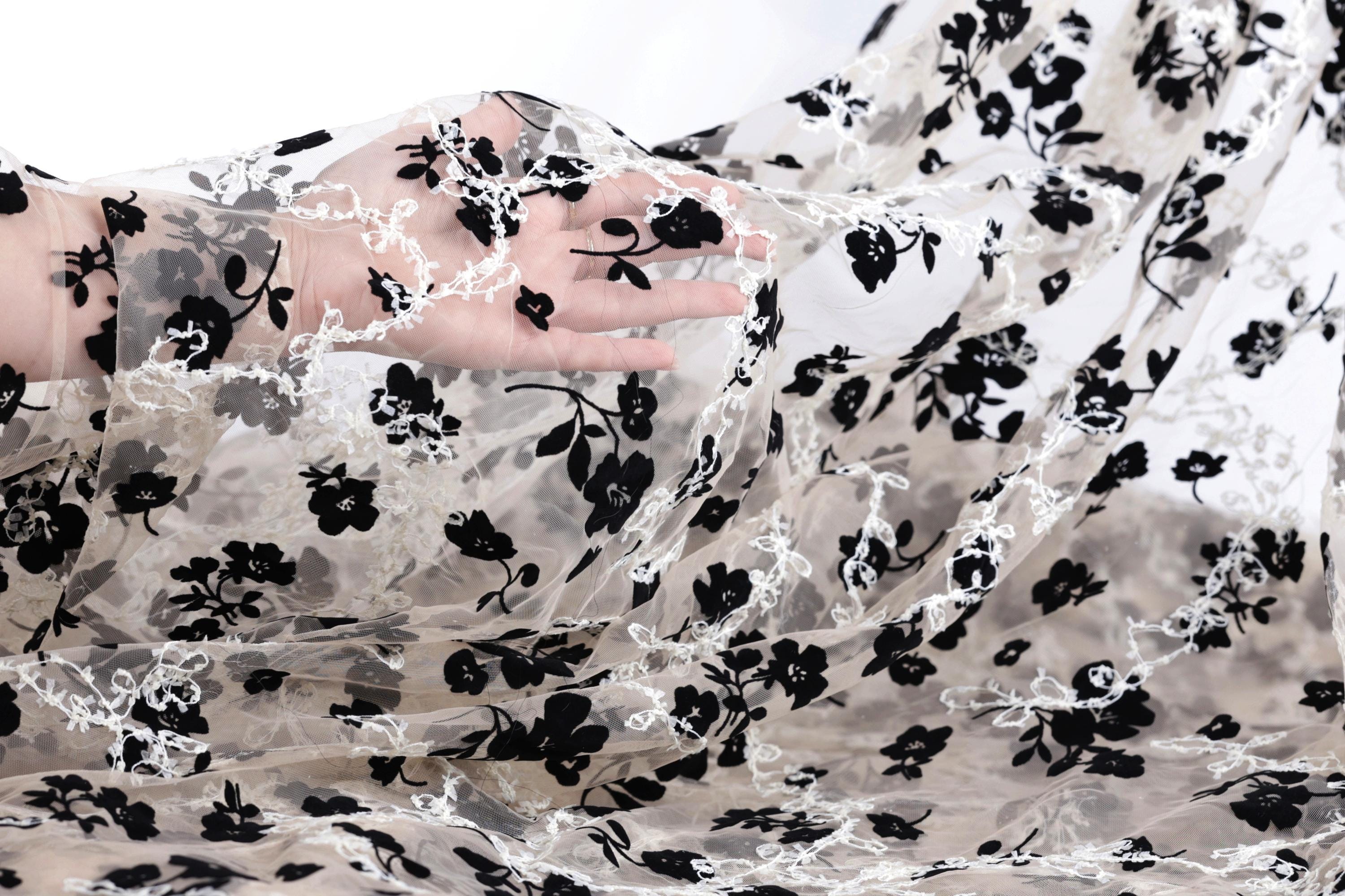 A hand is holding a piece of sheer fabric with a black and white floral pattern.