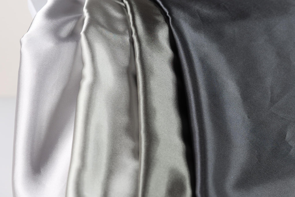 a close-up view of three different colored satin fabrics, with the first fabric being white, the second being silver, and the third being black.