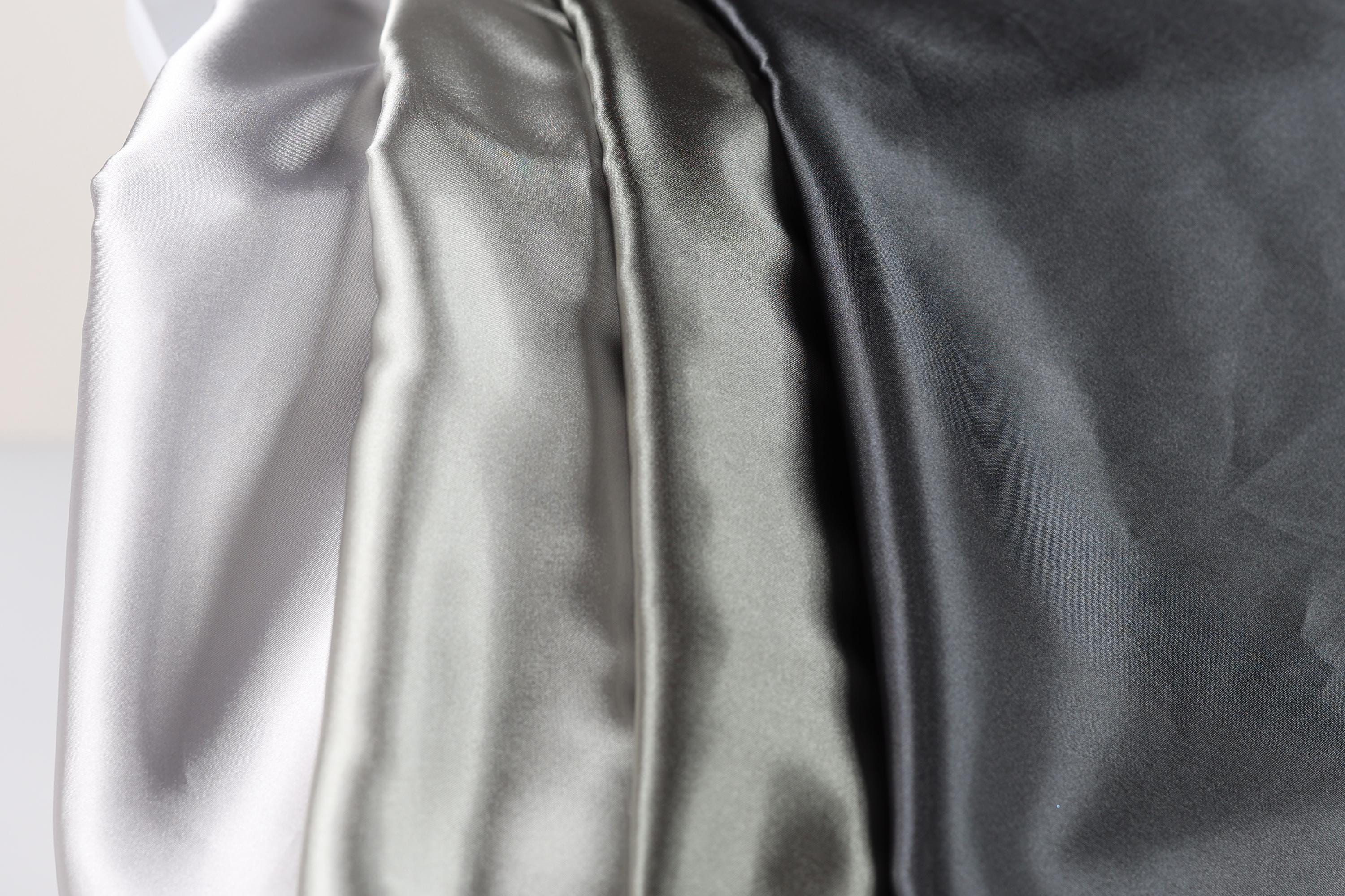 a close-up view of three different colored satin fabrics, with the first fabric being white, the second being silver, and the third being black.