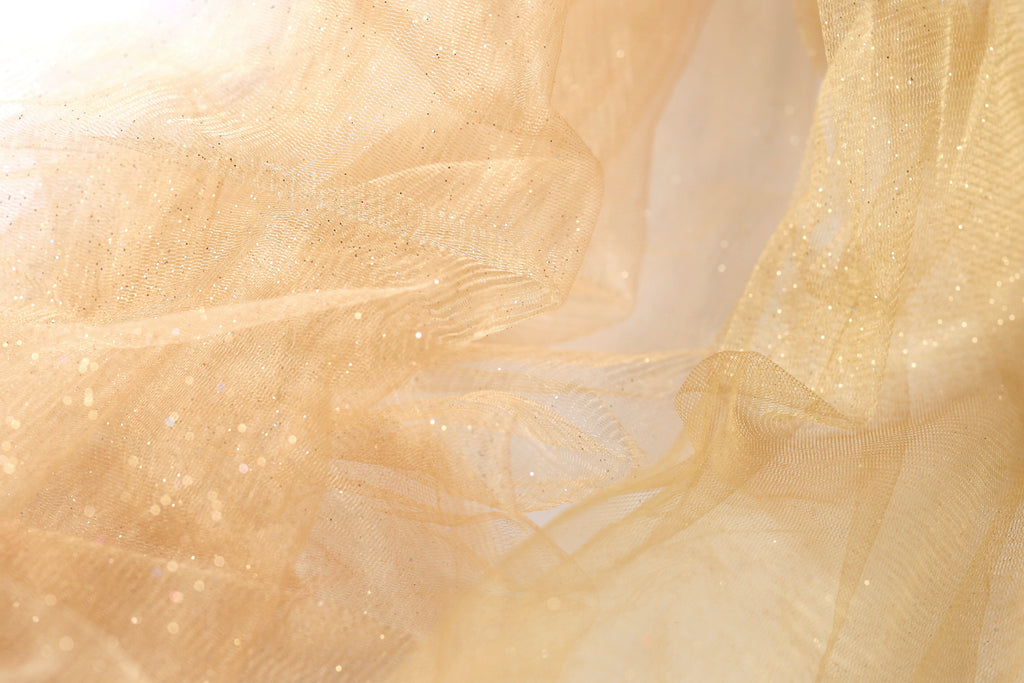 The image is a close-up of a light brown fabric with a shimmering, sparkly texture.