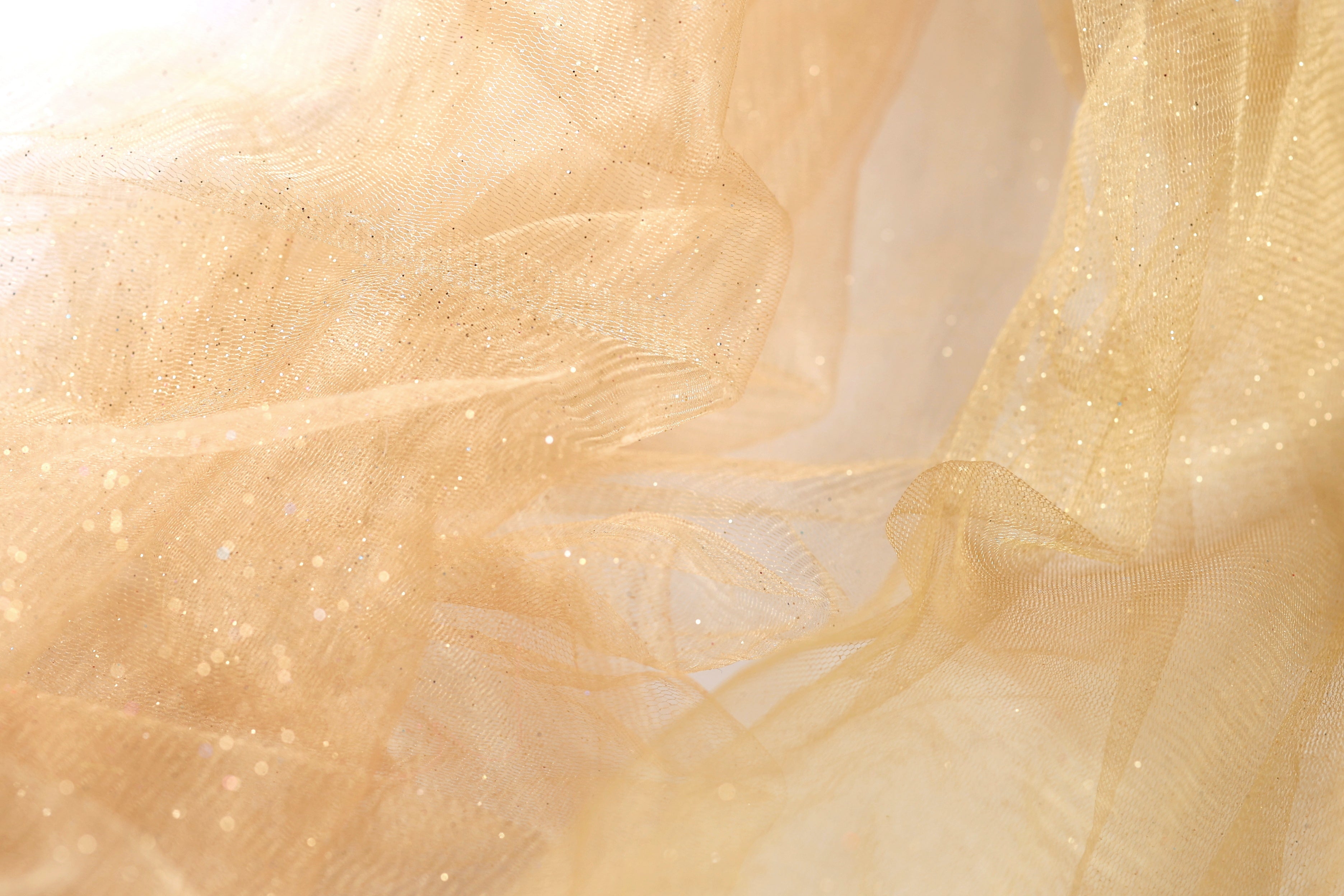 The image is a close-up of a light brown fabric with a shimmering, sparkly texture.