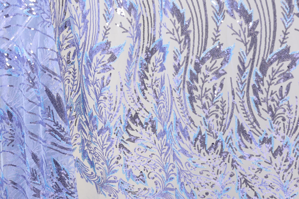 a close-up view of a fabric with a repeating pattern of purple and white sequin designs. The pattern appears to be a floral or leaf-like design, with the sequins adding a touch of sparkle and texture to the fabric. The fabric is predominantly white, with the purple and white sequins creating a visually striking contrast. The image does not contain any text or other discernible objects, and the focus is solely on the intricate and detailed pattern of the fabric.