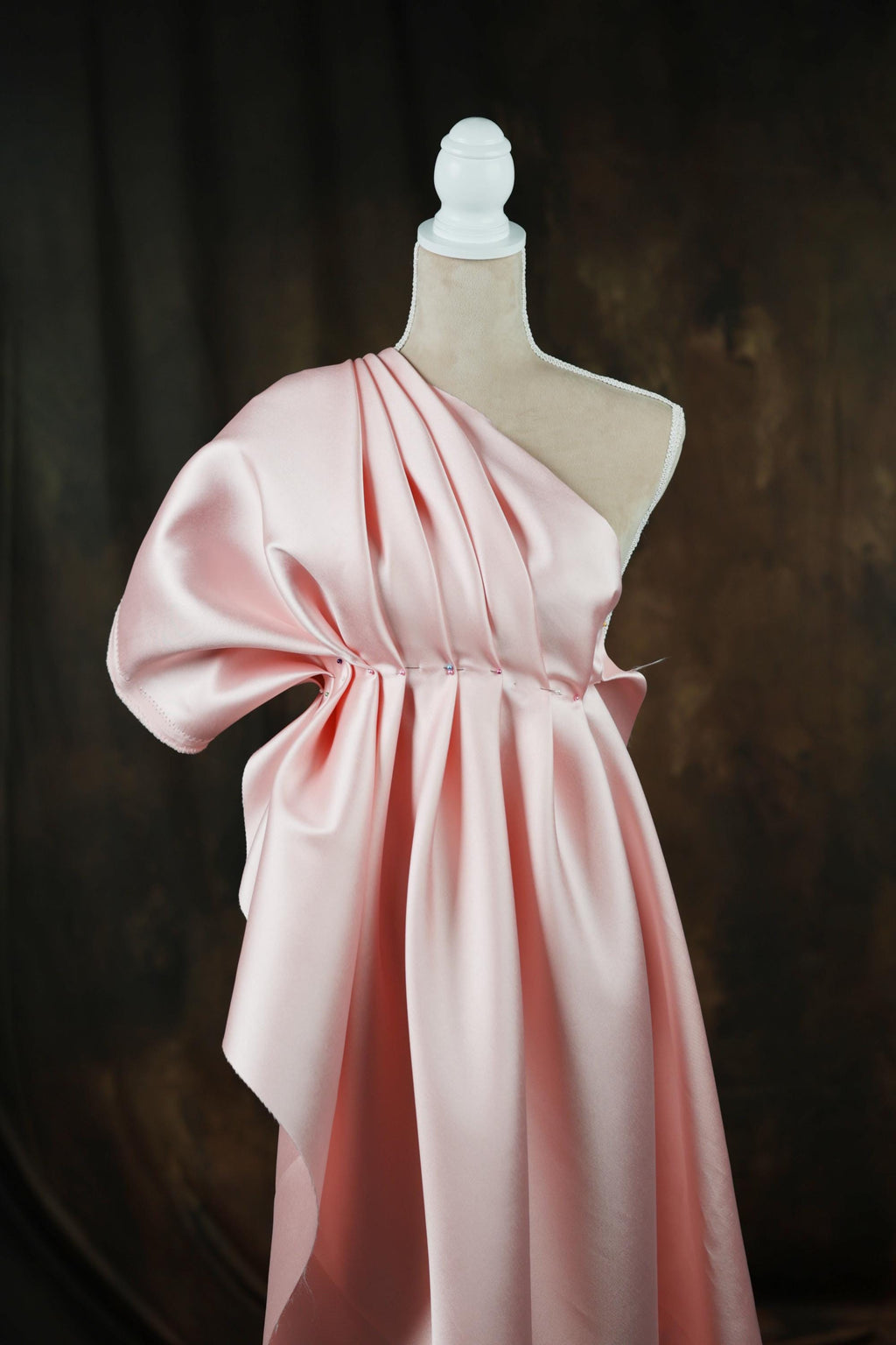 A pink one-shoulder dress displayed on a mannequin against a dark background.