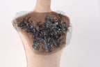 A mannequin with a decorative black lace or beaded floral pattern on its chest area.