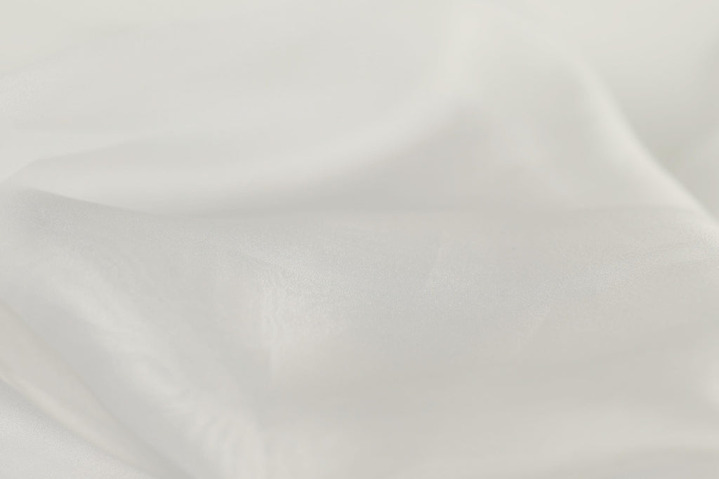The image is a close-up of a white fabric, possibly silk or chiffon, with a soft, flowing texture.