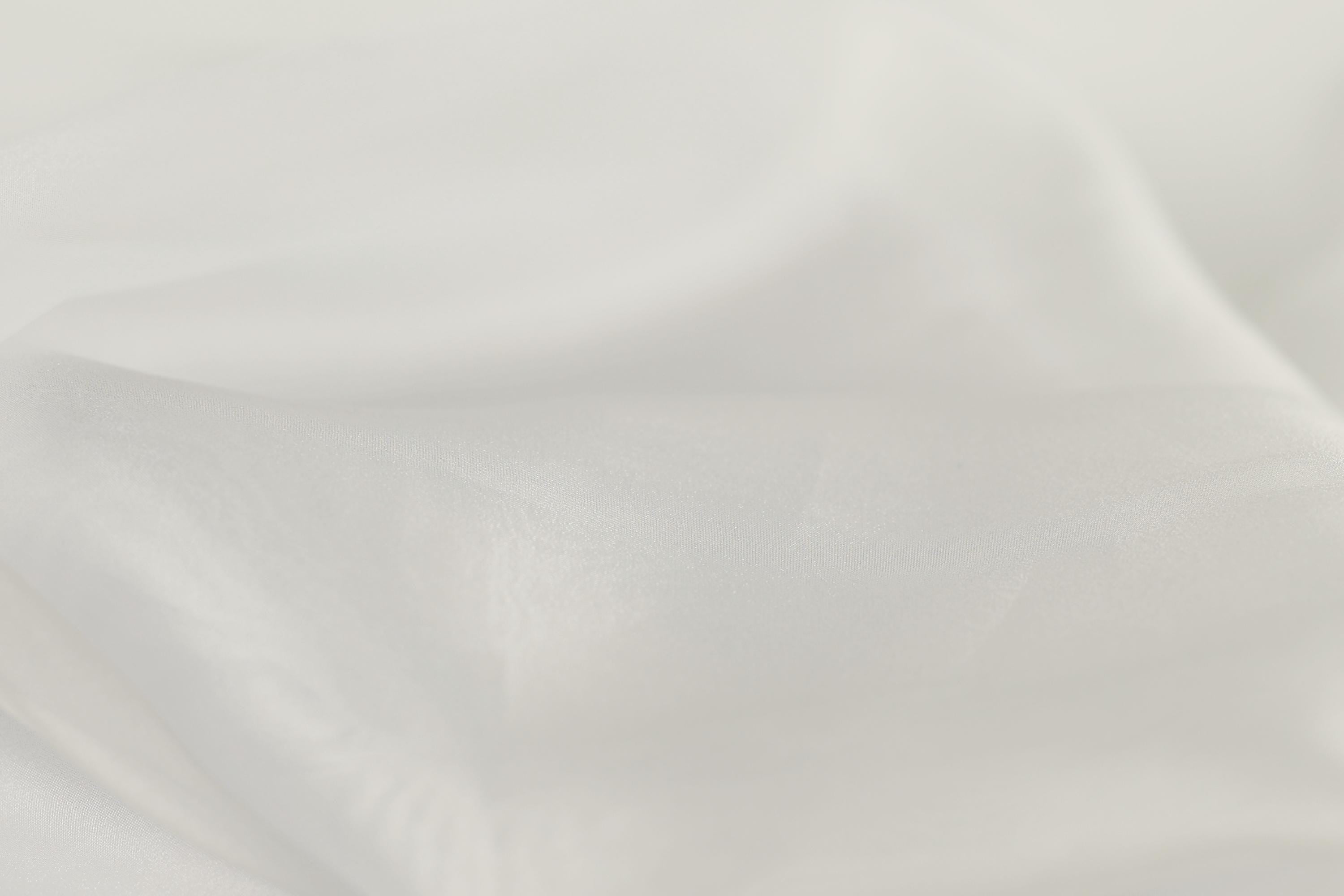 The image is a close-up of a white fabric, possibly silk or chiffon, with a soft, flowing texture.