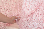 A hand is holding a piece of fabric with a pink floral pattern, which appears to be a close-up view of the fabric.