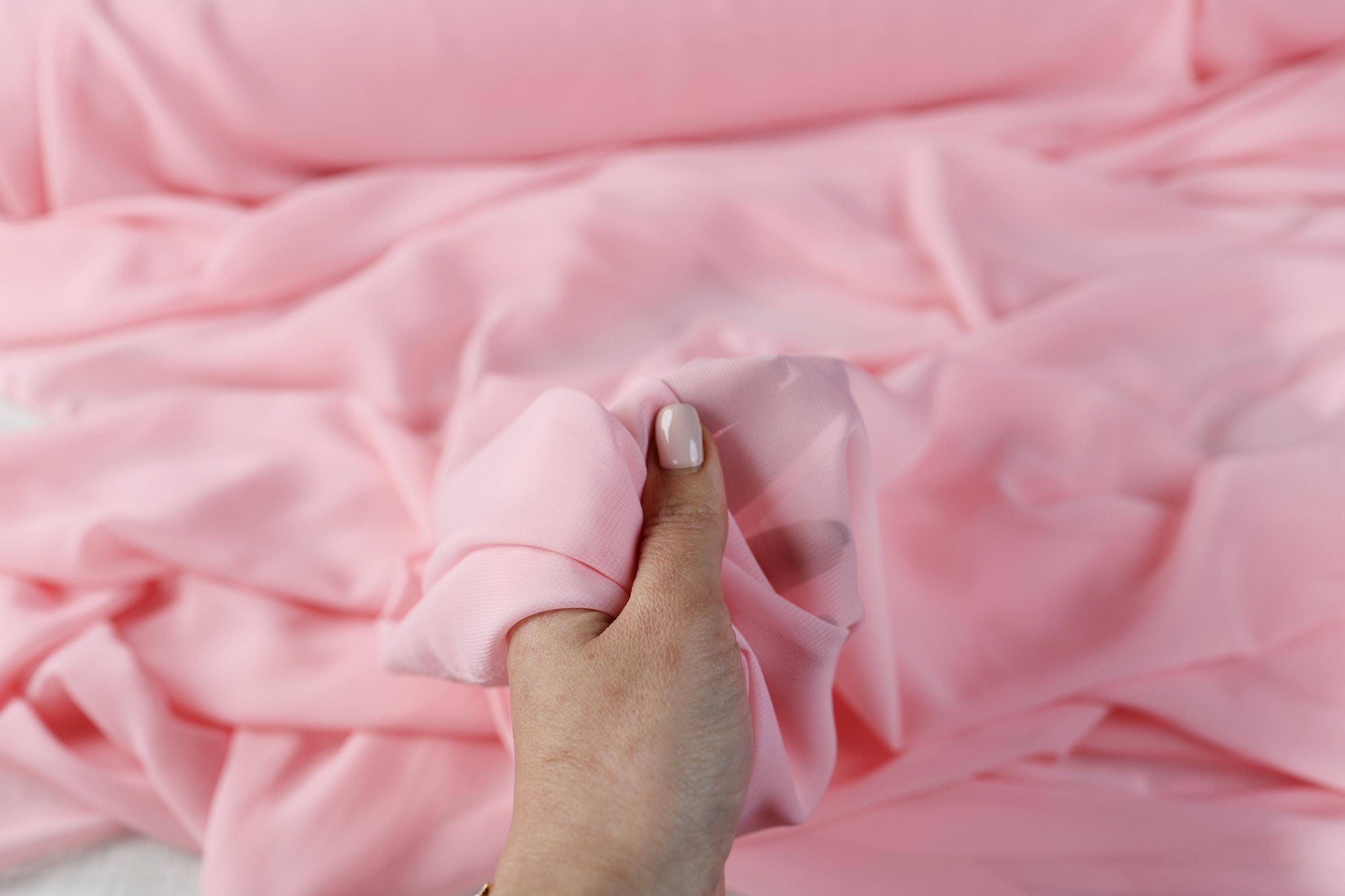 a person holding a pink cloth over a bed