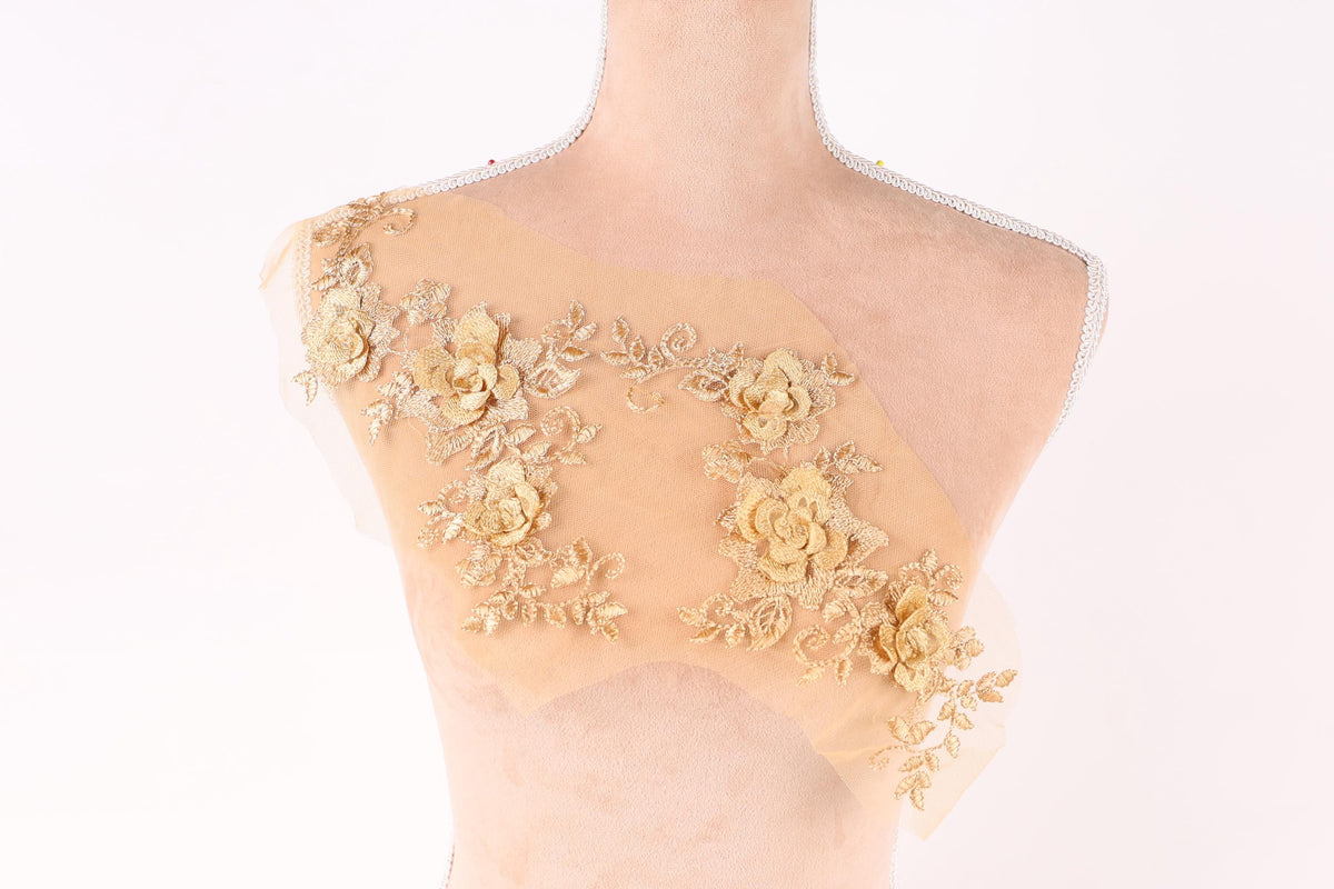 A mannequin torso with a beige fabric adorned with delicate gold floral embroidery.