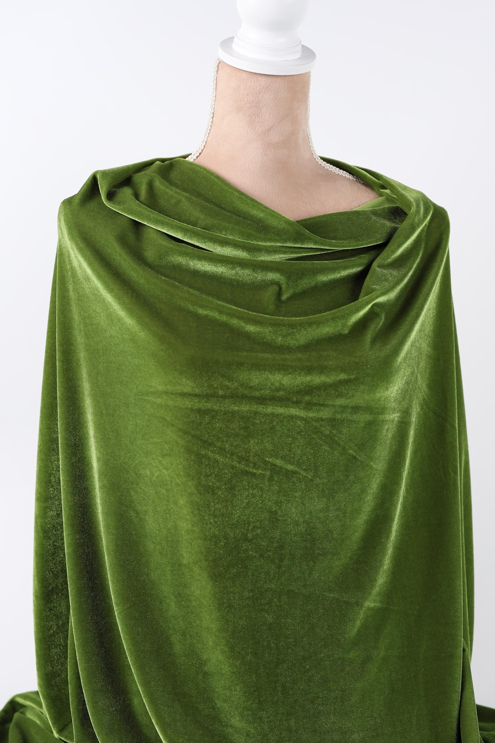 A close-up view of a green velvet fabric, with a white hand visible in the background.