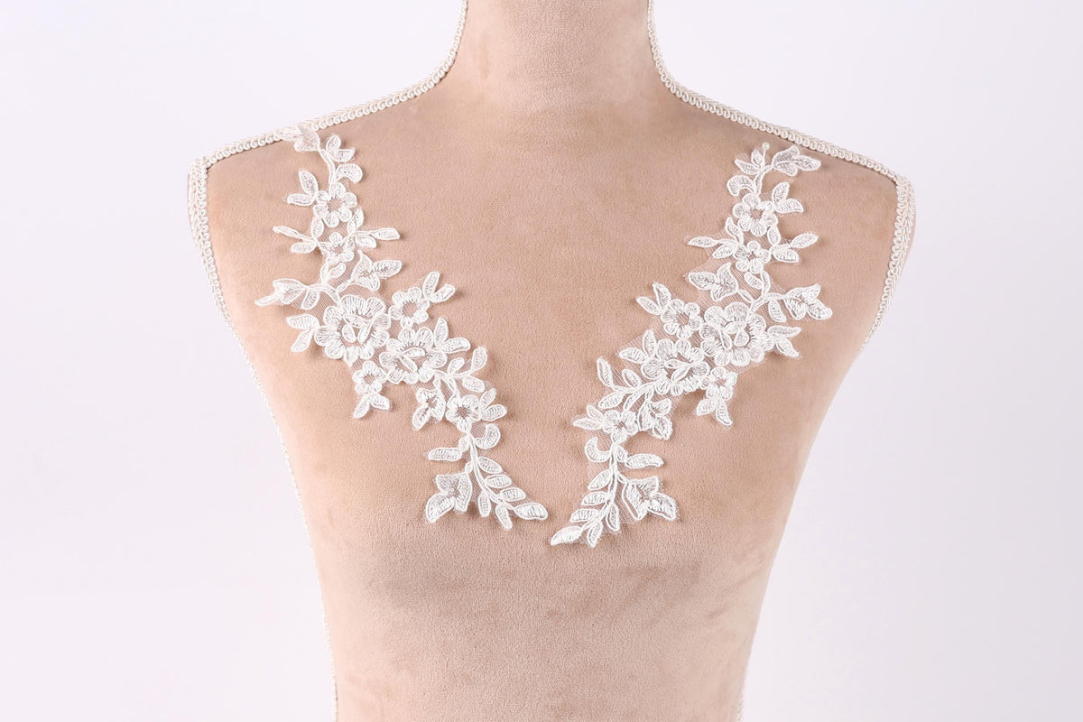 A mannequin wearing a white lace dress with delicate floral embroidery on the shoulders.