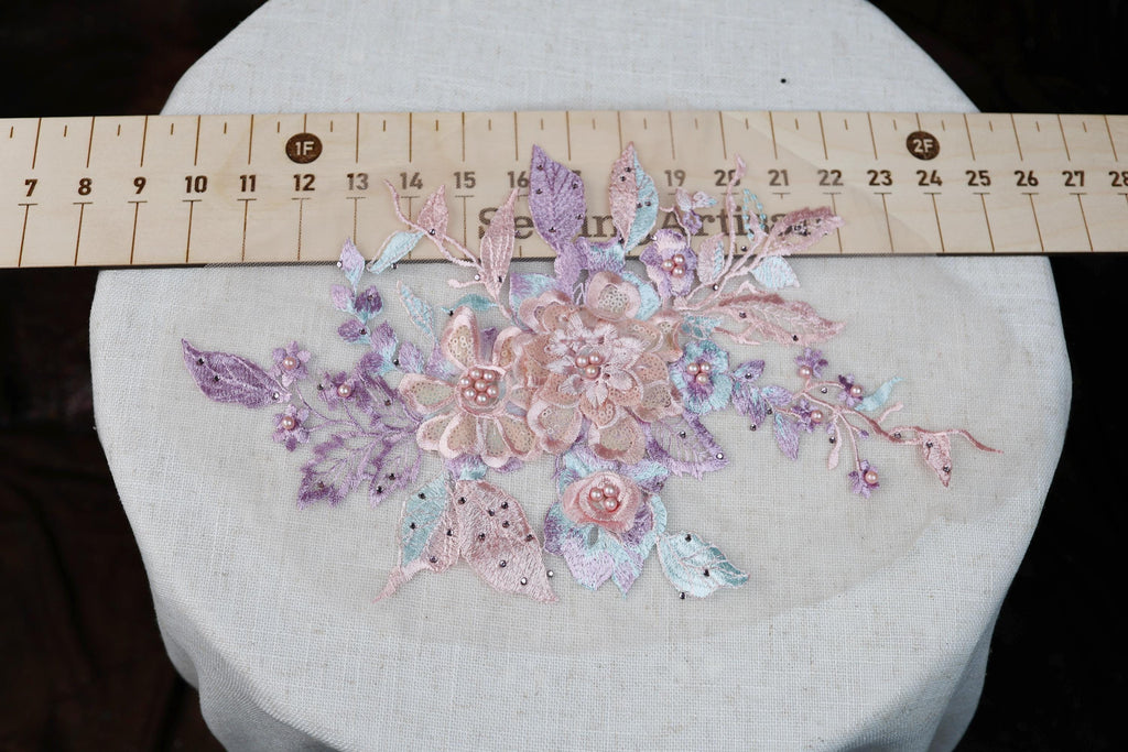 a close-up view of a delicate floral embroidery on a white fabric, with a ruler placed over it to provide a size reference.